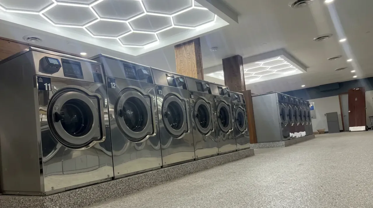 Row of stainless Wascomat Touch front-load washers beneath a hexagonal LED ceiling feature in a modern Minnesota laundromat